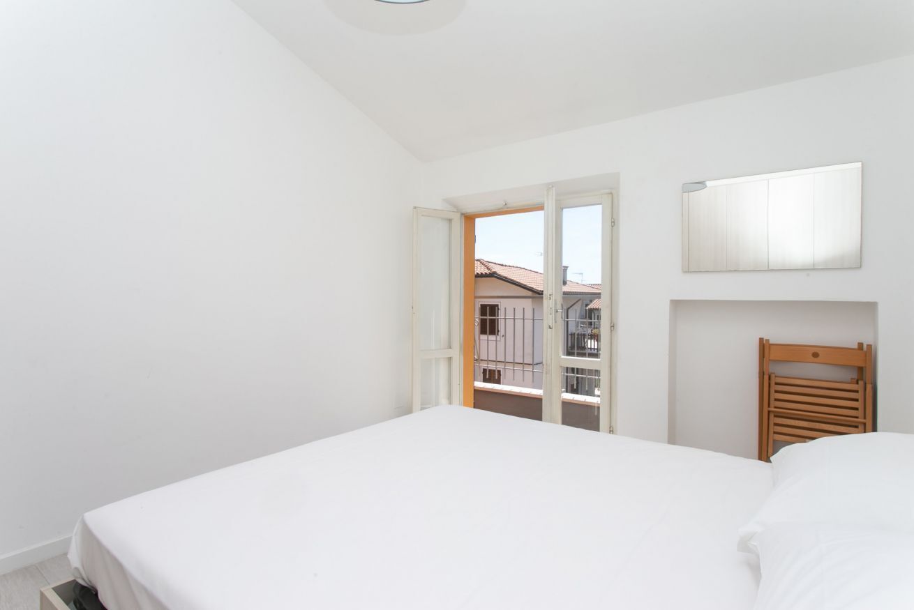 A bedroom with a bed, a wooden headboard, a window with a view of buildings, and a door leading outside.