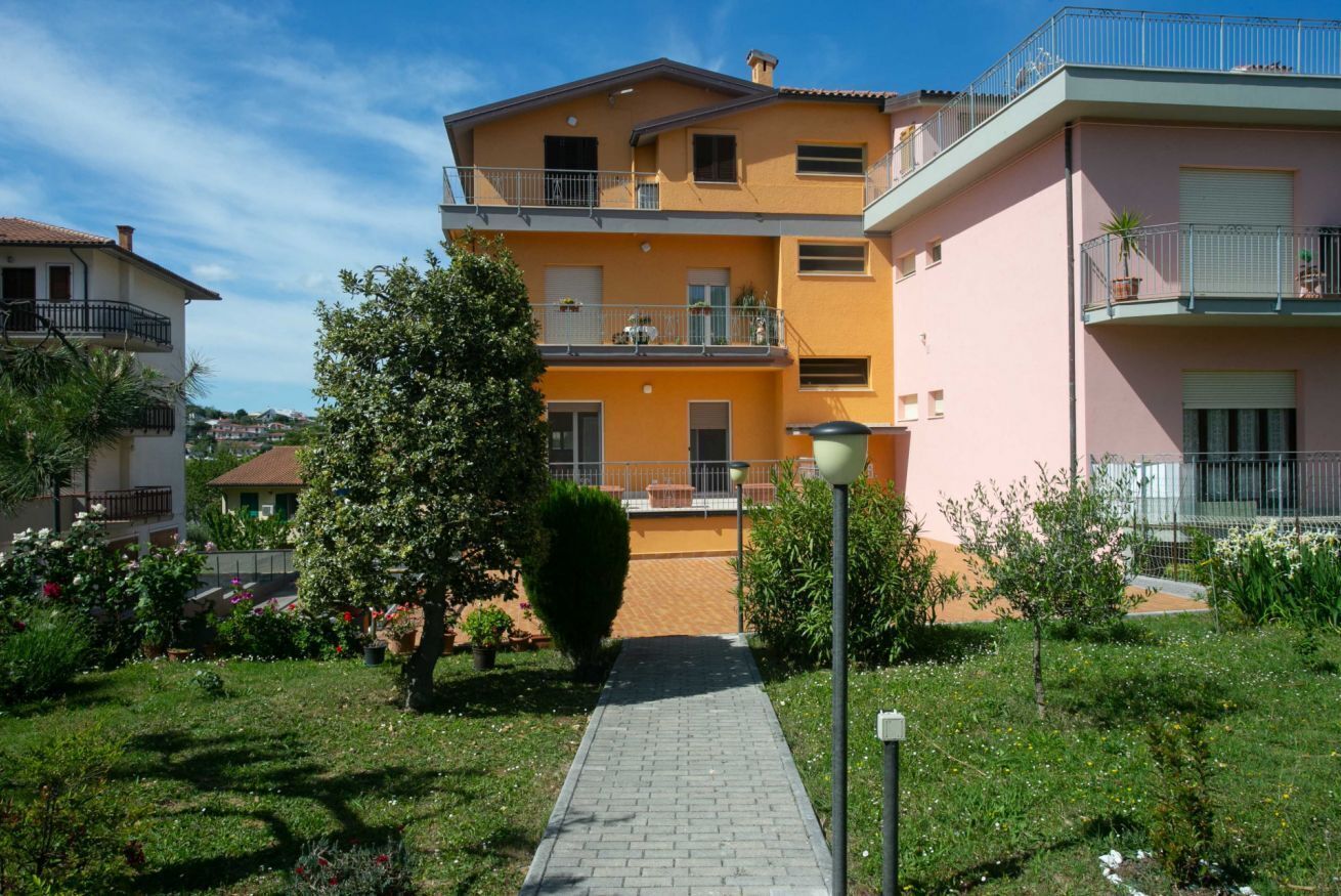 A multi-story residential building with balconies, a paved pathway, and a garden area.