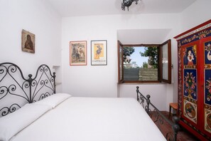 A bedroom with a bed, a window, a chair, and a decorative cabinet.