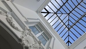 Een dakvenster met een geometrisch patroon, een witte muur met decoratieve lijstwerk en een raam met geëtste glas.