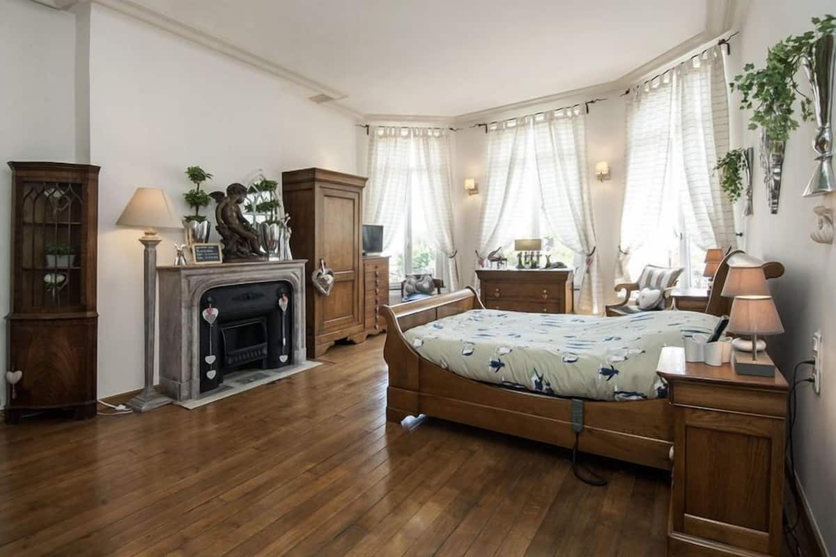 A bedroom with a wooden bed, a fireplace, a desk with a lamp, and a wardrobe.