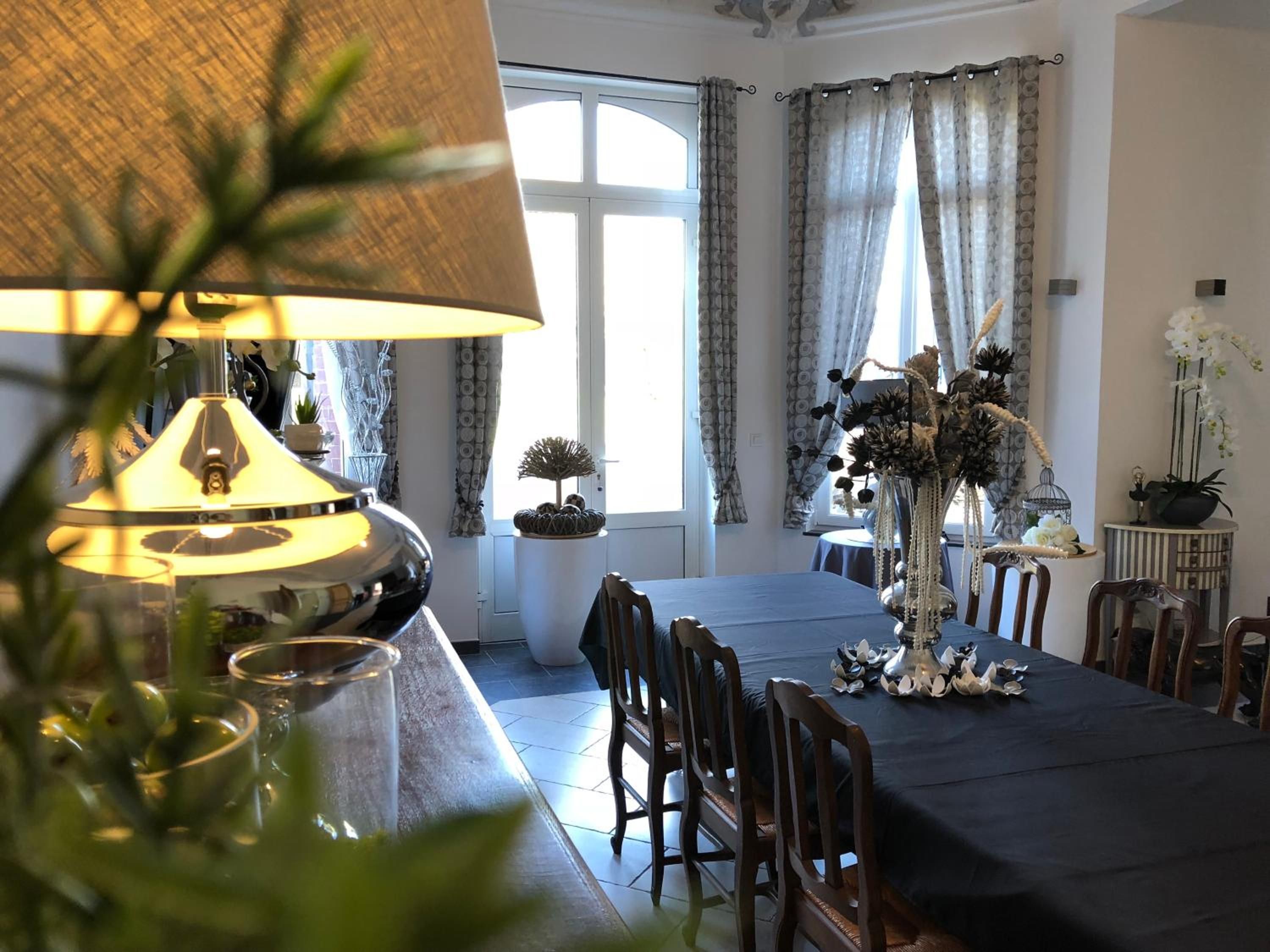 Une salle à manger avec une table dressée pour quatre personnes, une lampe et un vase rempli de fleurs.