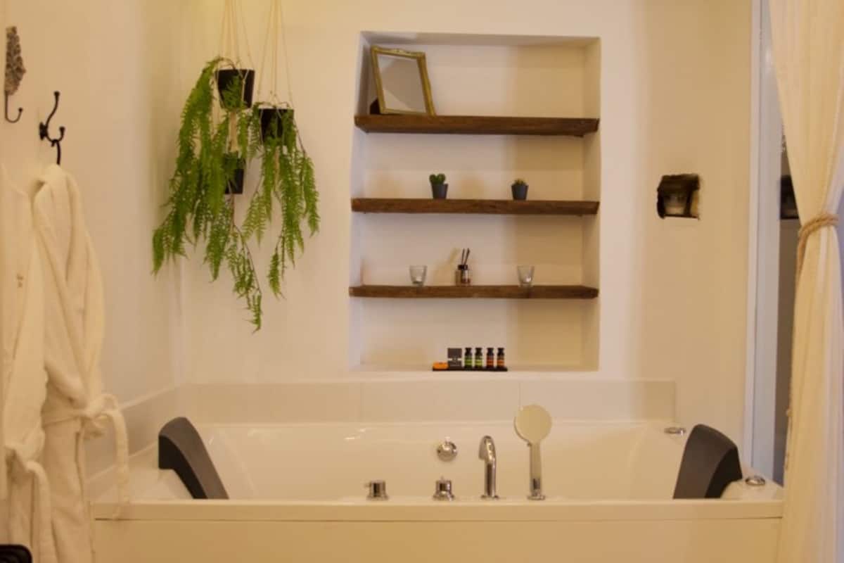 Ein Badezimmer mit einer Badewanne, Ablagen für Pflegeprodukte, einer hängenden Pflanze und einem Handtuchhalter.