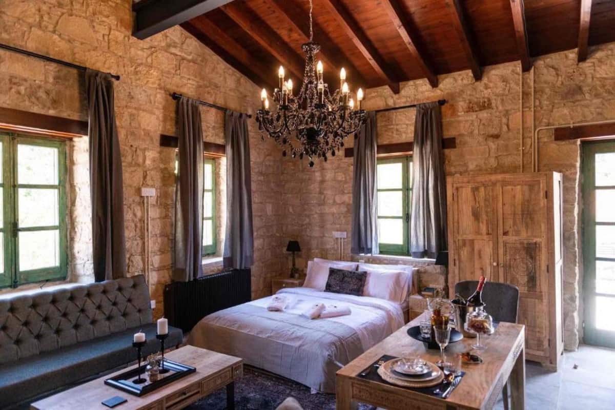Ein rustikaler Raum mit Steinwand, einem großen Bett, einer Chandelierleuchtre und einem für zwei Personen gedecktem Esstisch.