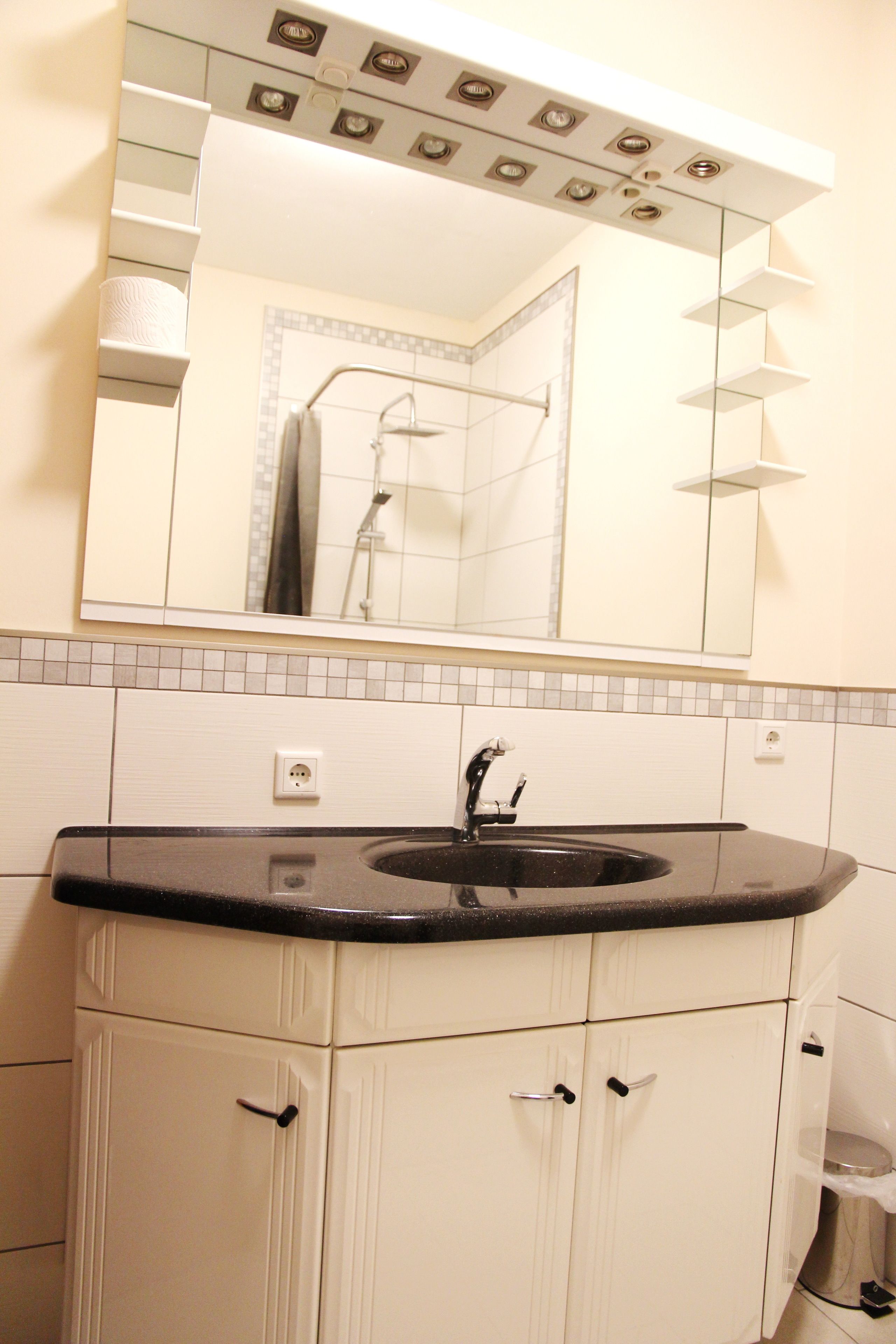 A bathroom with a white vanity, a black sink, and a mirror above the mirror.