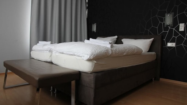 A modern bedroom with a large bed, a bench, and a dark wall with a geometric pattern. - Apartment Caplex (Oldenburg)