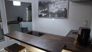 A compact kitchen with a dark countertop, a built-in stove, and a coffee maker. - Apartment Caplex (Oldenburg)