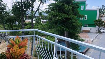 A balcony with a potted plant, a white railing, and a view of a green building and trees.