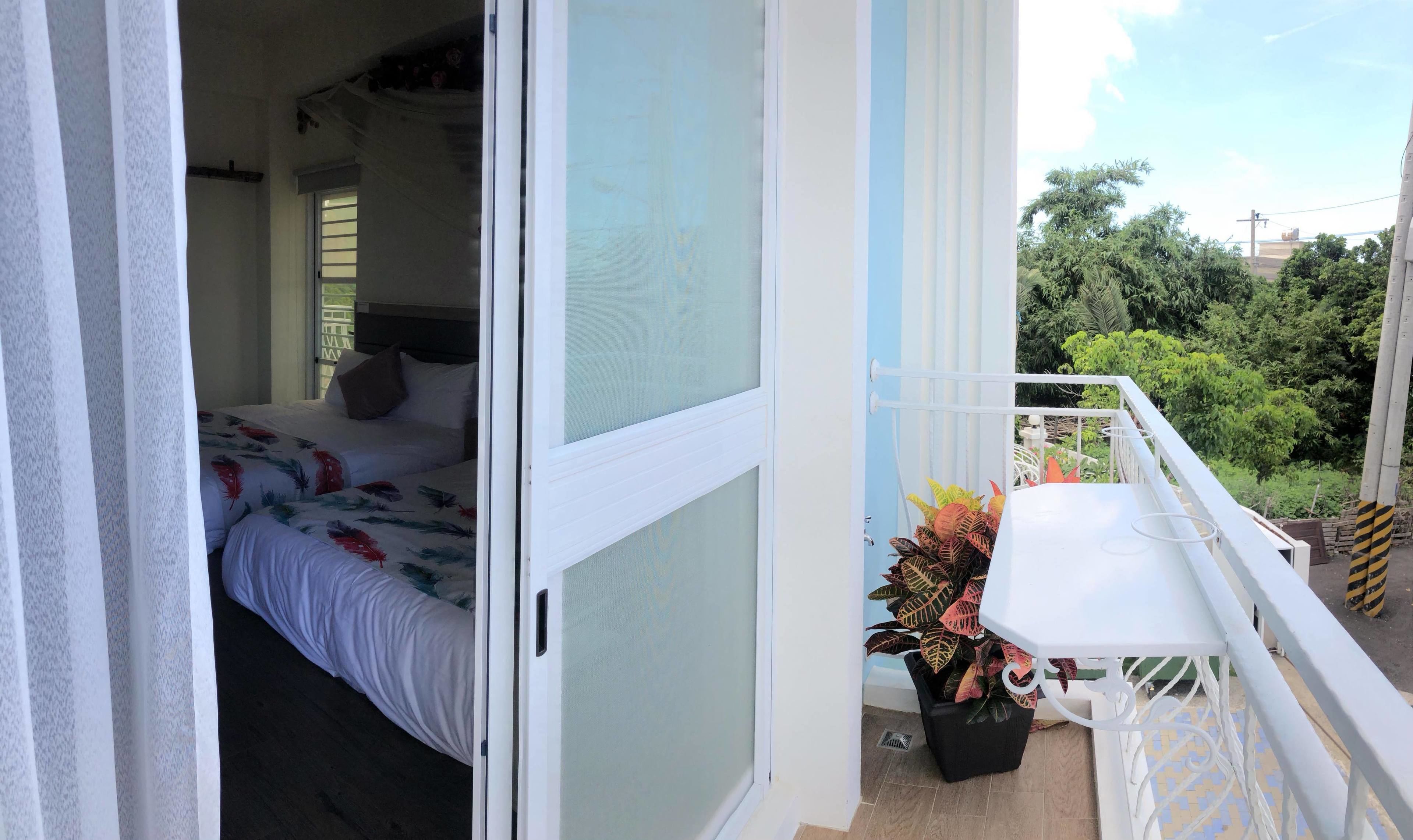 A bedroom with a bed, a window, and a balcony with a table and potted plant.