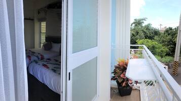 A bedroom with a bed, a window, and a balcony with a table and potted plant.