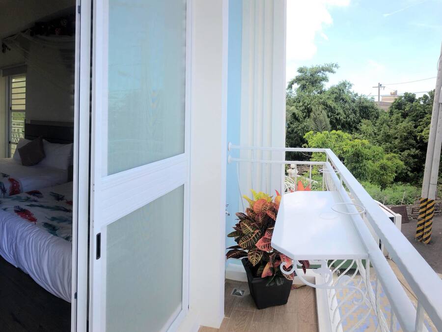 A bedroom with a bed, a window, and a balcony with a table and potted plant.