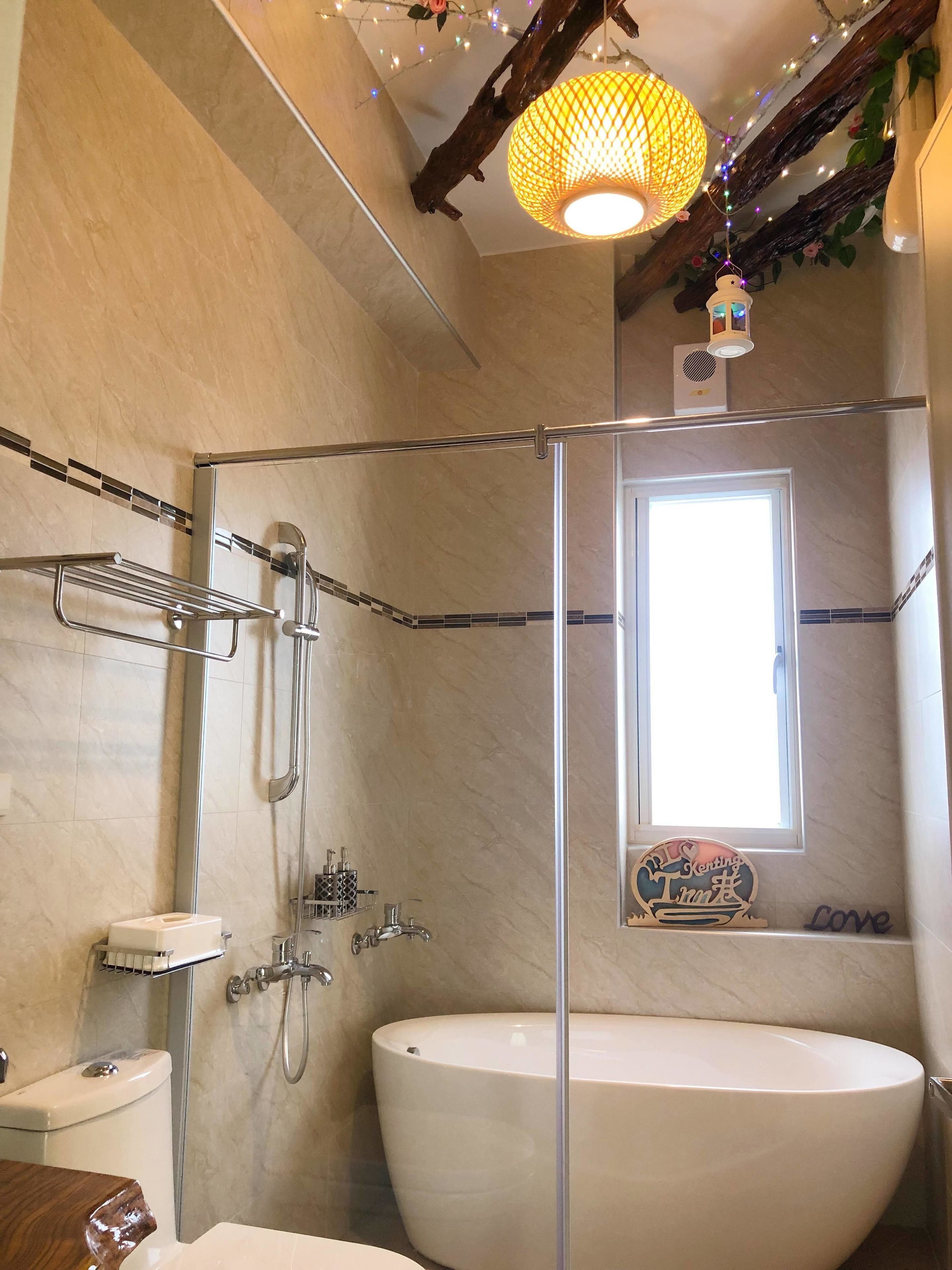A bathroom with a glass-enclosed shower, a large white bathtub, a toilet, and a window with a decorative sign.