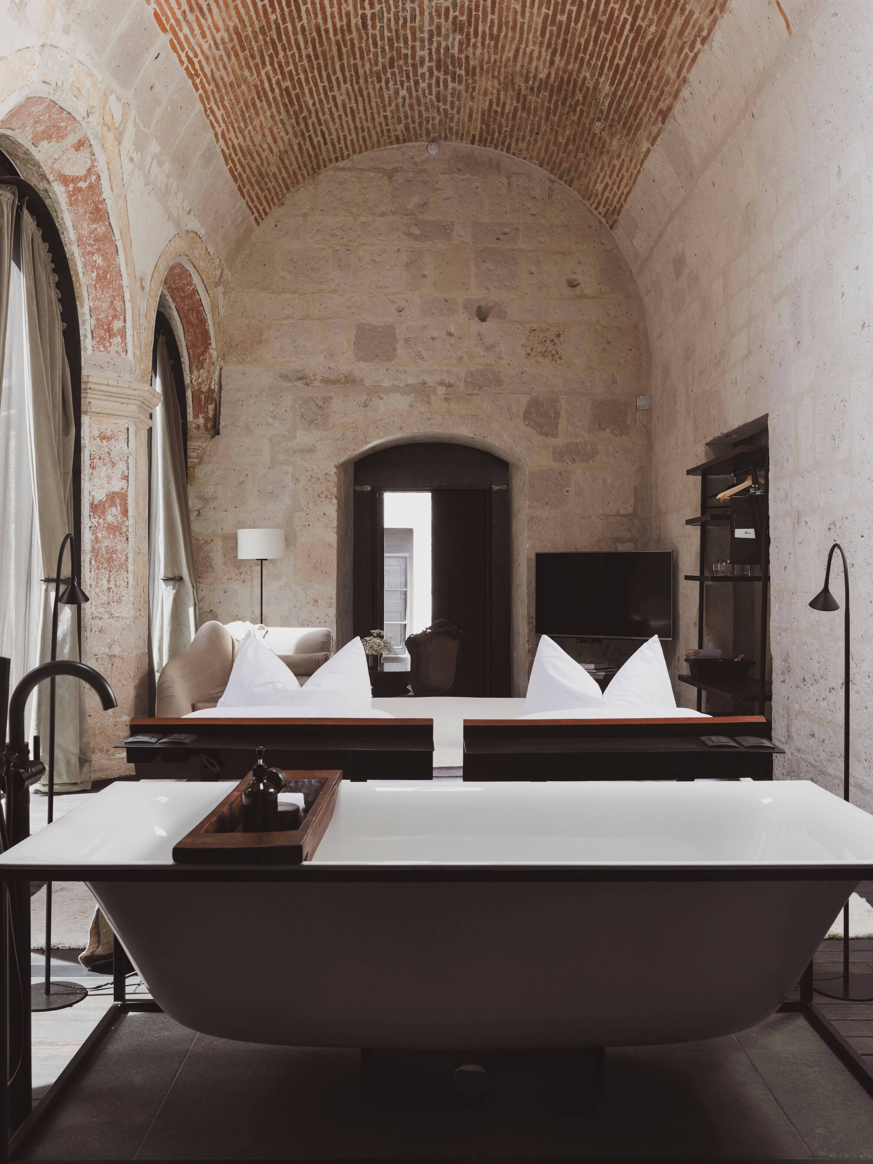 A room with a large bathtub, a sofa, a TV, and a lamp.