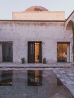 A building with a pool, a dome, and two open doors leading to interior spaces.