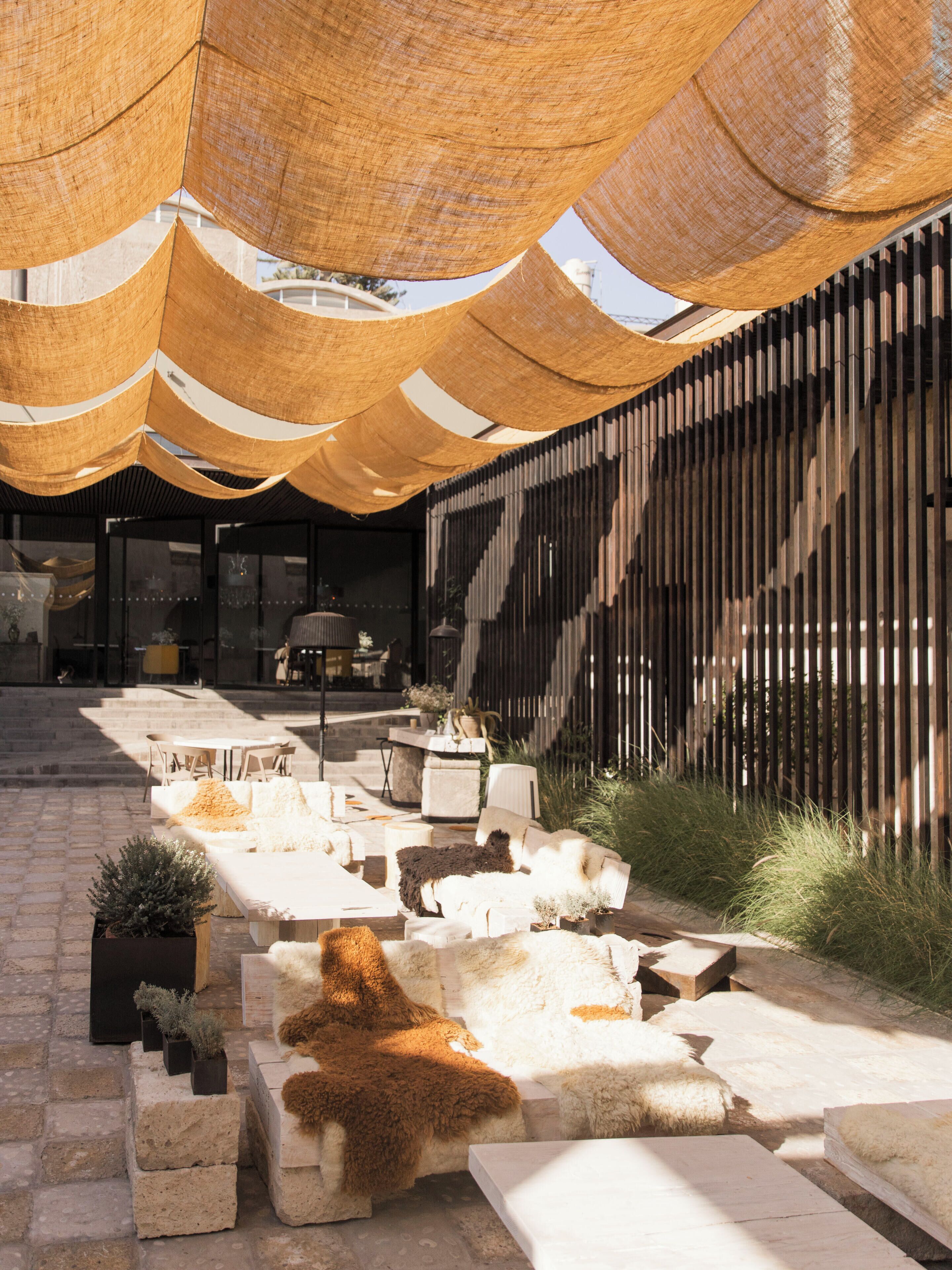 Un espace extérieur aménagé avec un design moderne, comprenant un mélange de canapés et de fauteuils, une clôture en bois et une structure en forme de pergola.