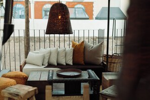Un espace de détente extérieur accueillant, avec un luminaire suspendu en osier, des sièges confortables dotés de coussins et un panier en osier.