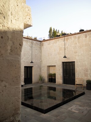 Un patio con piscina, muros de piedra y luces colgantes.