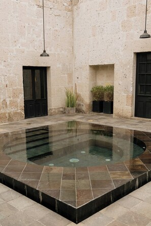 A stone-walled courtyard with a central pool, black doors, and potted plants. - CIRQA by Andean (Arequipa)