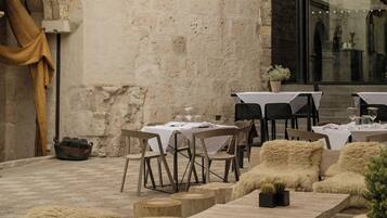 Un área de comedor al aire libre con mesas y sillas, una rústica pared de piedra y un ventanal grande.