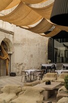 An outdoor dining area with tables and chairs, a rustic stone wall, and a large window.