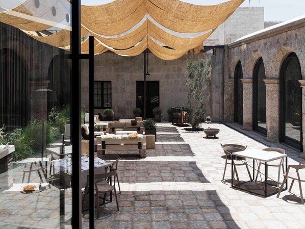 Un patio exterior con suelo de piedra, mobiliario de madera y un amplio toldo.