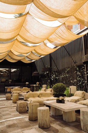 A modern outdoor seating area with wooden tables and chairs, a stone floor, and a canopy overhead. - CIRQA by Andean (Arequipa)