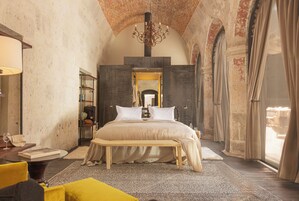 A bedroom with a large bed, a bench, a bedside table, and a chandelier.