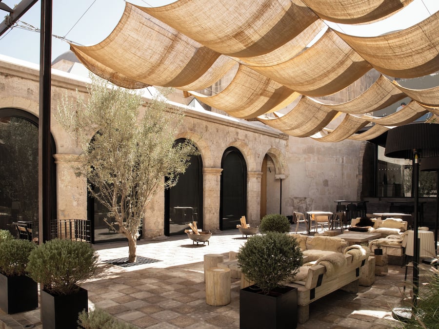 Un espacio al aire libre con mesas, sillas, un árbol y un edificio con arcos.