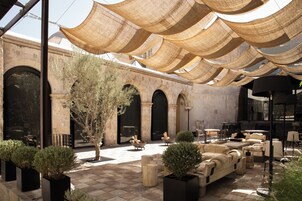 An outdoor seating area with tables and chairs, a tree, and a building with arches.