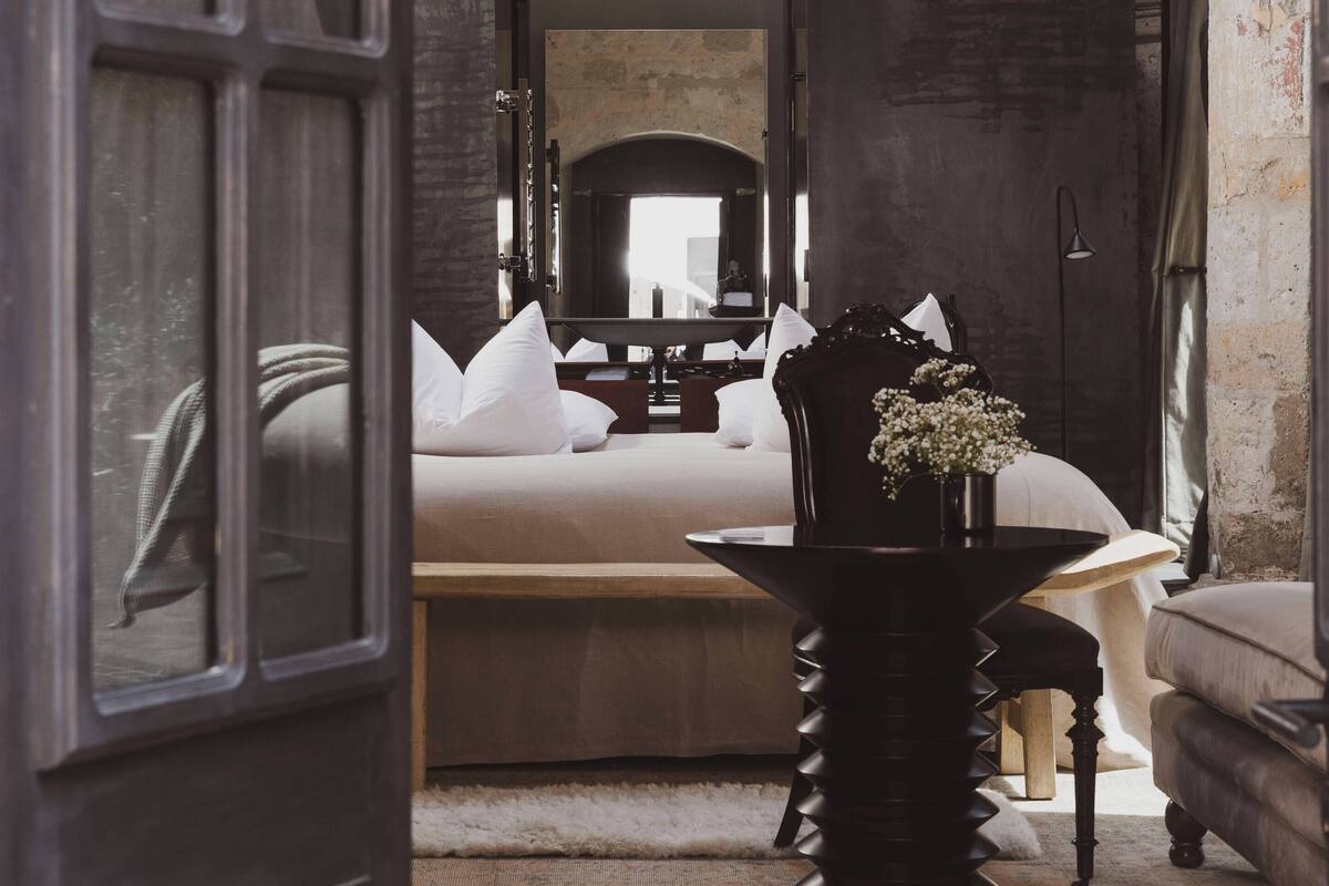 Ein Zimmer mit einem Bett, einem Tisch mit einer Vase und einer Chandelüster.