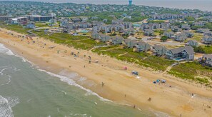 An aerial view of a coastal residential area with houses, a beach, and a lighthouse.