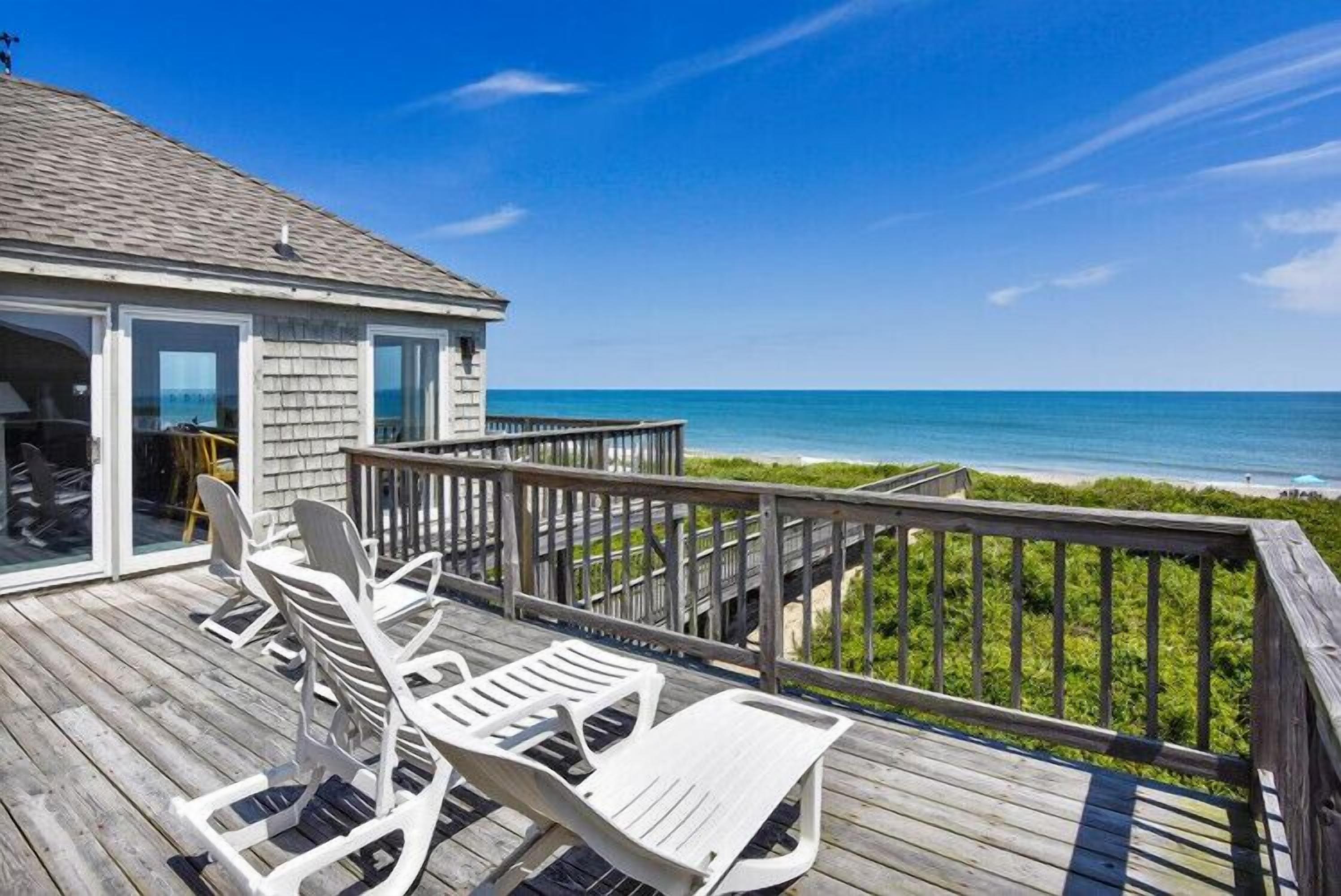 A wooden deck with outdoor furniture overlooking a beach.