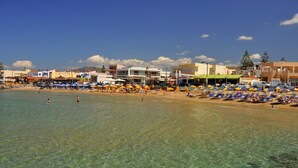 Ein Strand mit klarem Wasser, Sonnenschirmen und Liegestühlen.