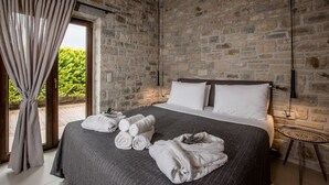 Ein Schlafzimmer mit Steinwand, einem Bett mit weißen Bettwäsche und Blick durch eine Glastür.