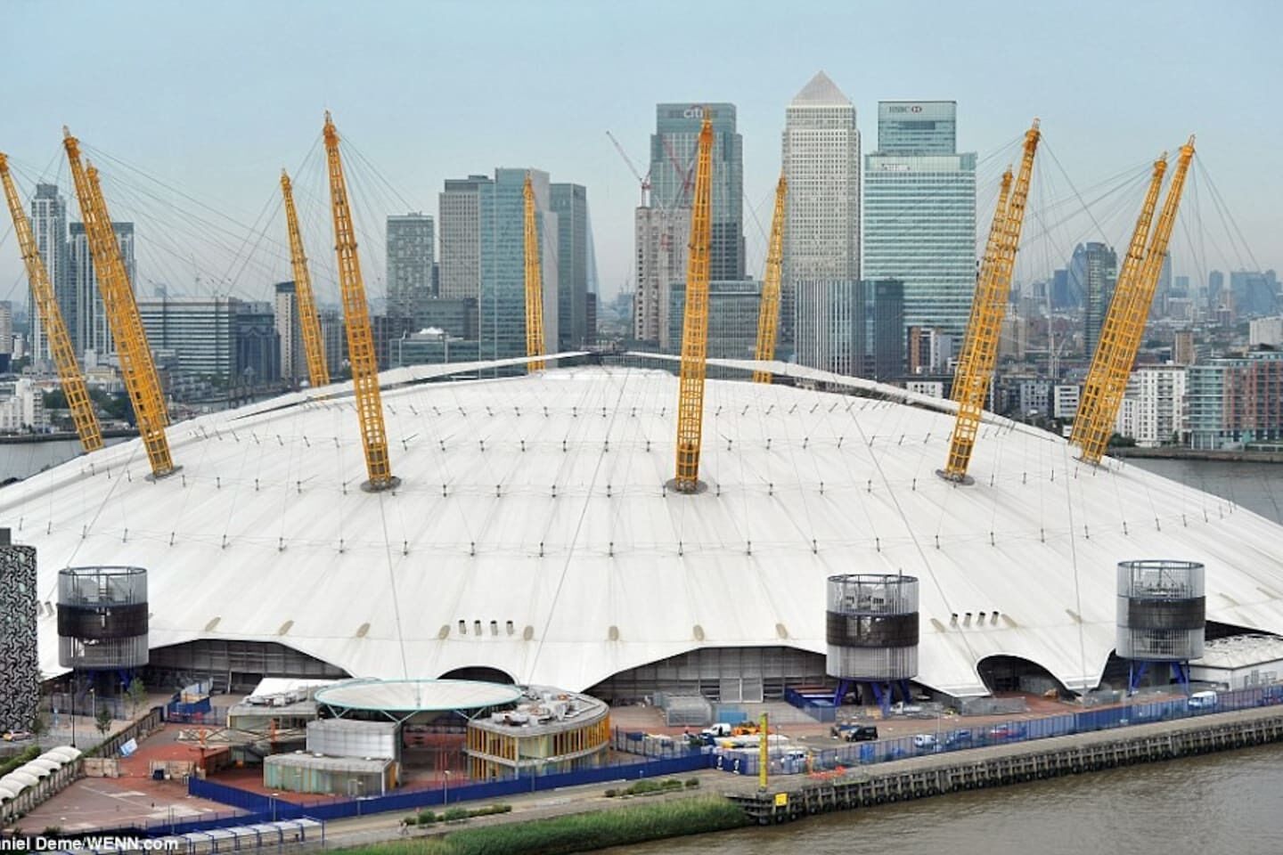 A large stadium with a white roof and multiple cranes, surrounded by high-rise buildings.