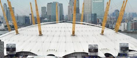 A large stadium with a white roof and multiple cranes, surrounded by high-rise buildings.