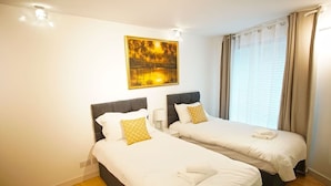 A hotel room with two beds, a painting on the wall, and a window with curtains. - Superior Canary Wharf  O2 Arena 2Bed Apartment (Greater London)