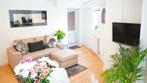 A modern living room with a beige sofa, a flat-screen TV, and a potted plant. - Superior Canary Wharf  O2 Arena 2Bed Apartment (Greater London)