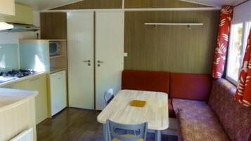 Une cuisine compacte équipée d’une cuisinière, d’un réfrigérateur et d’un petit évier. On y trouve une table à manger avec deux chaises et un banc avec un coussin.