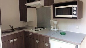 Cozinha compacta com fogão a gás, micro-ondas e um frigorífico pequeno.