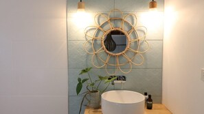 Une salle de bain avec un miroir rond, un lavabo blanc, une décoration murale et une plante en pot.