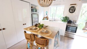 Une cuisine moderne avec des meubles blancs, un îlot central agrémenté de sets de table en fibres tressées, des chaises en osier et un luminaire suspendu.