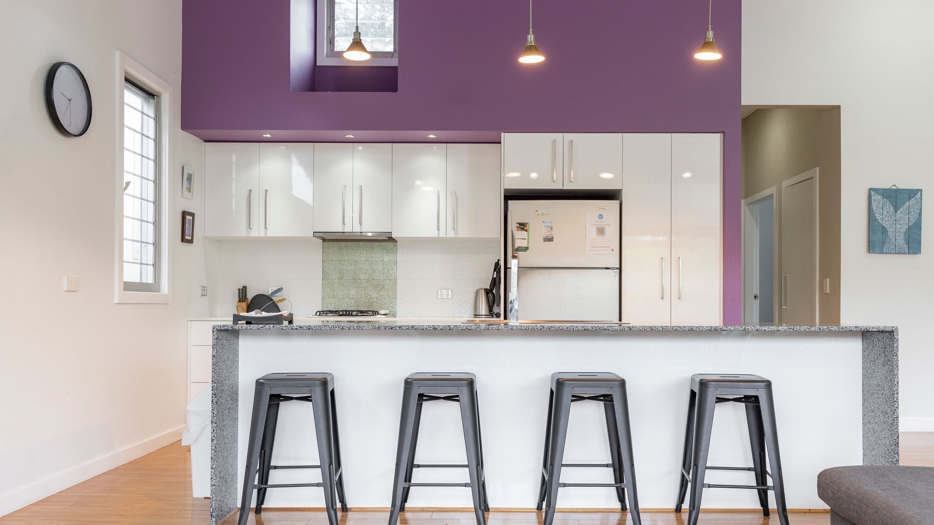A modern kitchen with white cabinets, a granite countertop, and three black bar stools.