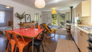 A modern kitchen with wooden cabinets, a dining area with orange chairs, and a cozy seating area with a yellow chair. - Pippis - a Classic Beach House (Seal Rocks)