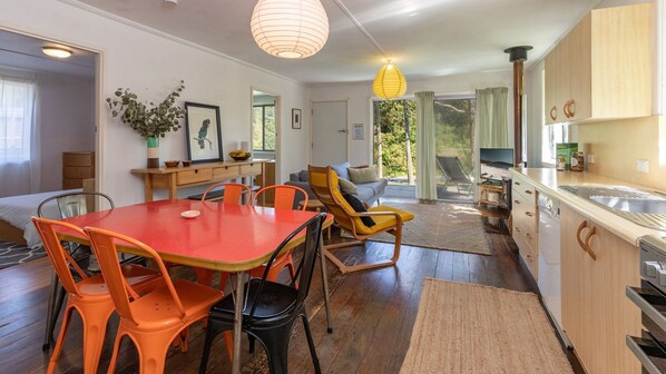 Eine moderne Küche mit Holzausstattung, ein Essbereich mit orangefarbenen Stühlen und eine gemütliche Sitzecke mit einem gelben Sessel.