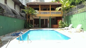Una piscina con sillas de descanso y un edificio de dos pisos con balcones.