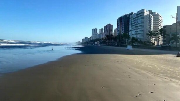 Una playa con cielo despejado, una orilla arenosa y edificios altos al fondo.