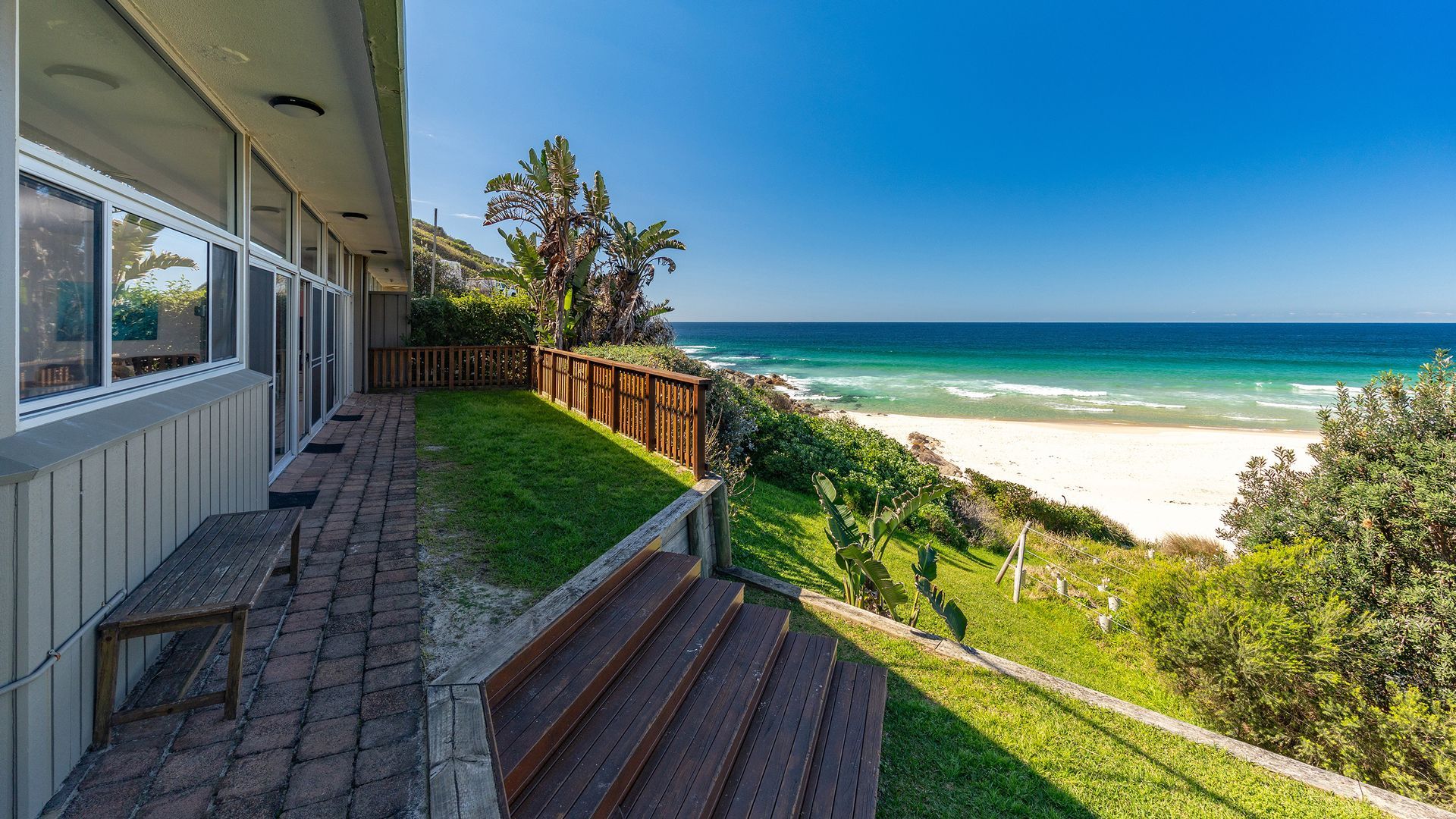 A coastal property with a wooden deck, a view of the ocean, and a sandy beach.