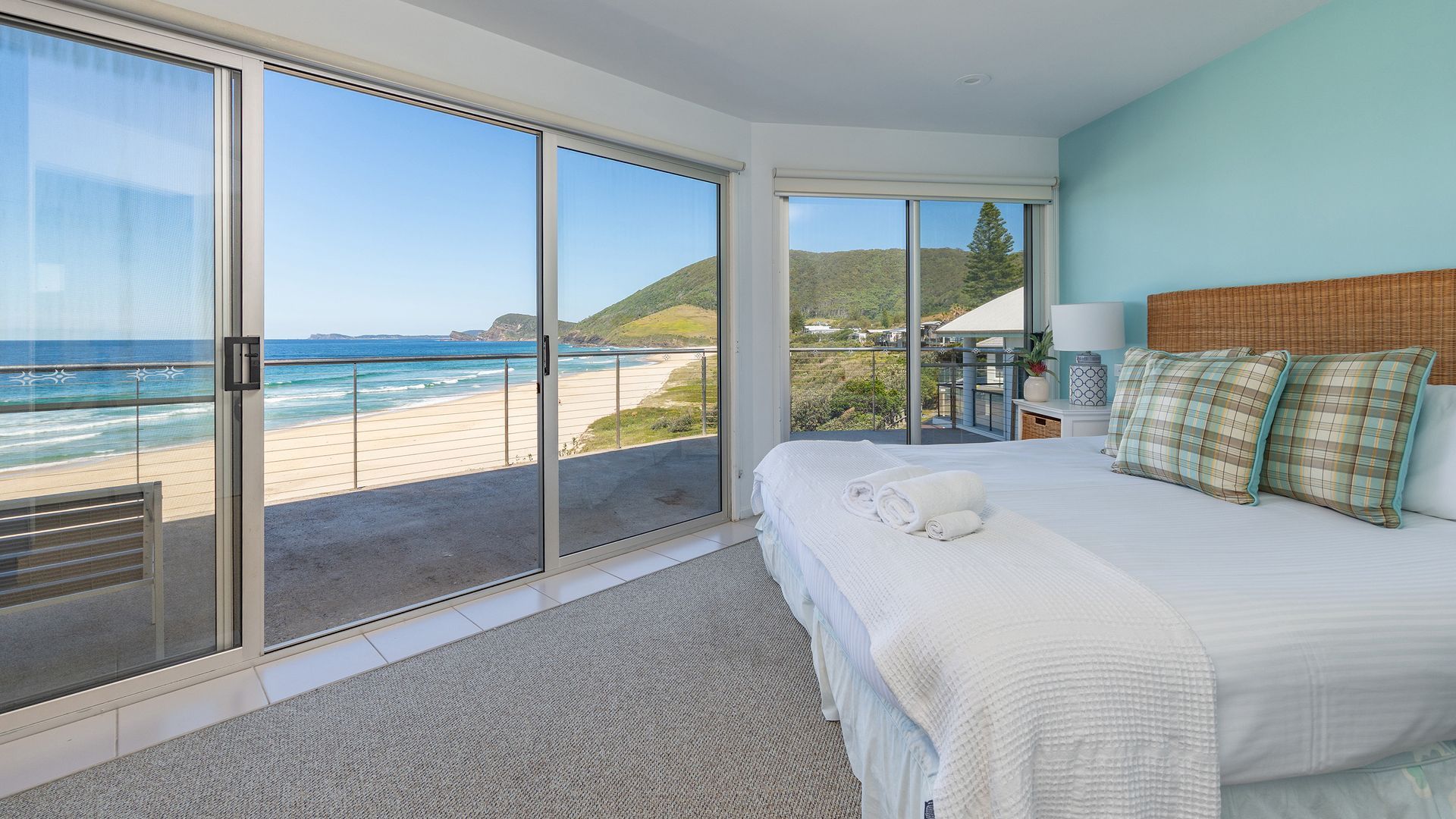 A bedroom with a large sliding glass door leading to a balcony with a beach view.