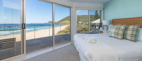 Ein Schlafzimmer mit einer großen Schiebeglastür, die auf einen Balkon mit Blick auf den Strand führt.